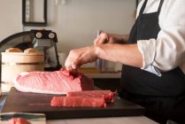 Vista laterale di ritagliato irriconoscibile usato chef maschio taglio di pesce crudo a tavola nel ristorante asiatico e preparare sushi — Foto stock