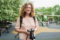 Окаменелая женщина-фотограф с современной камерой стоит в зеленом парке и смотрит в сторону — стоковое фото
