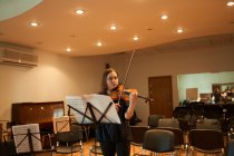 Músico feminino profissional tocando violino acústico e olhando para a folha de música durante o ensaio em estúdio — Fotografia de Stock