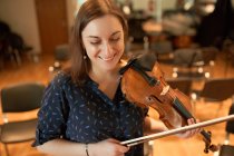 Весела професійна жінка-музикантка грає на акустичній скрипці і дивиться на музичний аркуш під час репетиції в студії — стокове фото