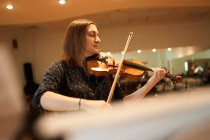 Сосредоточенная профессиональная женщина-музыкант играет на акустической скрипке с закрытыми глазами с нотами во время репетиции в студии — стоковое фото
