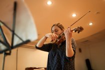 Músico profissional focado tocando violino acústico com os olhos fechados com folha de música durante o ensaio em estúdio — Fotografia de Stock