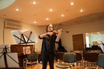 Konzentrierte professionelle Musikerin spielt akustische Geige bei geschlossenen Augen mit Notenblatt während der Probe im Studio — Stockfoto