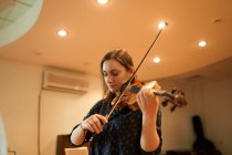 Konzentrierte professionelle Musikerin spielt akustische Geige bei geschlossenen Augen mit Notenblatt während der Probe im Studio — Stockfoto
