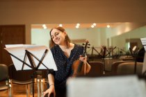 Cheerful professional female musician playing acoustic violin and looking at music sheet during rehearsal in studio — Stock Photo