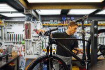 Technicien masculin concentré attachant la roue au vélo tout en travaillant dans un atelier professionnel moderne — Photo de stock