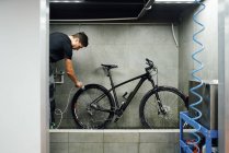 Vista lateral de la caja de engranajes de limpieza mecánica masculina de rueda de bicicleta con agua en el taller - foto de stock