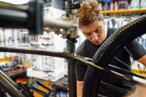 Орієнтований чоловічий технік прикріплює колесо до велосипеда під час роботи в професійній сучасній майстерні — стокове фото