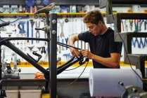 Konzentrierter männlicher Meister wischt Fahrradrahmen mit Lappen ab, während er in moderner Reparaturwerkstatt arbeitet — Stockfoto