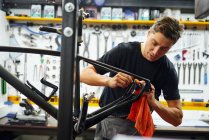 Konzentrierter männlicher Meister wischt Fahrradrahmen mit Lappen ab, während er in moderner Reparaturwerkstatt arbeitet — Stockfoto