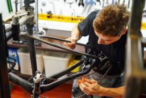 Focalisé mâle maître essuyant cadre de vélo avec chiffon tout en travaillant dans un atelier de réparation moderne — Photo de stock