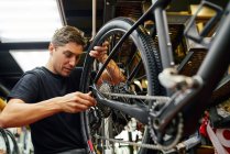 Technicien masculin attachant la roue au vélo tout en travaillant dans un atelier moderne professionnel — Photo de stock