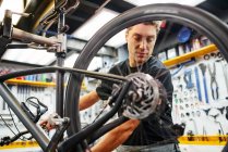 Männlicher Techniker montiert Rad an Fahrrad, während er in professioneller moderner Werkstatt arbeitet — Stockfoto