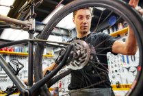 Male technician attaching wheel to bike while working in professional modern workshop — Stock Photo