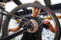 Чоловічий технік прикріплює колесо до велосипеда під час роботи в професійній сучасній майстерні — стокове фото