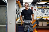 Glücklicher männlicher Mechaniker lächelt und blickt mit Werkzeug in Garage gegen Wand — Stockfoto