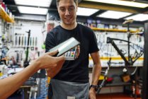Klient mit niedrigem Anbauwinkel bezahlt mit Smartphone an männlichen Techniker in Reparaturwerkstatt — Stockfoto