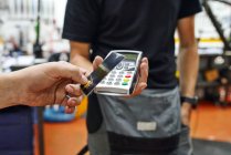Low angle of crop client using smartphone to pay to male technician in repair workshop — Stock Photo