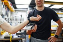 Soft focus of male mechanic with terminal receiving contactless payment from crop customer with smart watch during work in garage — Stock Photo