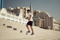 Vista lateral do atlético masculino correndo no andar de cima enquanto treina no dia ensolarado na cidade no verão — Fotografia de Stock