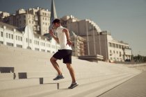 Vista lateral del atlético macho corriendo arriba mientras entrena en un día soleado en la ciudad en verano - foto de stock