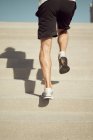 Вид ззаду на обрізаний невідомий атлетичний чоловік, що бігає нагору під час тренувань у сонячний день у місті влітку — стокове фото