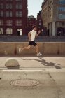 Seitenansicht eines starken männlichen Athleten, der im Sommer beim aktiven Training in der Stadt die Straße entlang springt — Stockfoto