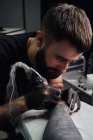 Concentrated male tattooist in gloves making tattoo on hand of client while using professional tattoo machine in modern tattoo studio — Stock Photo