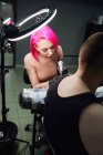 Серйозний майстер татуювання з рожевим волоссям в рукавичках з використанням професійного тату-машини при виготовленні татуювання на плечах клієнта в сучасному салоні татуювання. — стокове фото