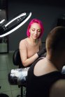 Мастер татуировки с розовыми волосами в перчатках, используя профессиональную тату-машину, делая татуировку на плече клиента в современном тату-салоне — стоковое фото
