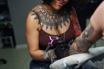 Tattoo master in gloves using professional tattoo machine while painting tattoo on arm of woman in modern tattoo studio — Stock Photo
