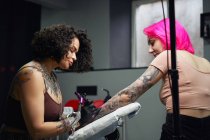 Tatuaggio master in guanti utilizzando la macchina professionale del tatuaggio mentre dipingi il tatuaggio sul braccio della donna nel moderno studio del tatuaggio — Foto stock