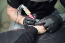 Konzentrierte männliche Tätowierer in Handschuhen machen Tätowierung auf der Hand des Kunden, während mit professionellen Tätowiermaschine in modernen Tätowierstudio — Stockfoto