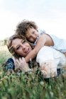 Side view of cheerful mother and curly haired little girl lying together on blanket in meadow and enjoying summer day — Stock Photo