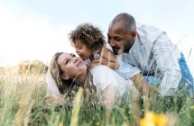 Side view of cheerful multiracial couple with adorable little daughter playing in meadow in summer — Stock Photo