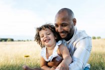 Afro-americano padre tenendo carino ricci capelli afroamericani figlia su sfondo di tramonto cielo in natura guardando altrove — Foto stock