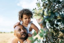 African American father and curious little daughter touching tree leaves in countryside in summer — Stock Photo