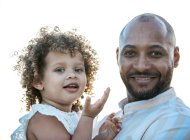 Afro-américain père tenant mignon frisé cheveux fille afro-américaine sur fond de coucher de soleil ciel dans la nature en regardant la caméra — Photo de stock