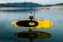 Вид сбоку на неузнаваемого серфера в гидрокостюме, стоящего с желтой доской SUP и веслом в морской воде — стоковое фото