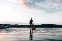 Von unten fokussierter männlicher Surfer, der bei Sonnenuntergang im Sommer auf dem SUP-Board auf ruhiger See schwimmt — Stockfoto