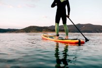 Cropped unrecognizable anonymous male surfer floating on SUP board on calm sea at sunset in summer — Stock Photo