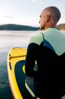 Back view of adult male in wetsuit kneeling on paddle board on calm lake water surface — Stock Photo