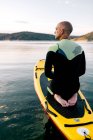 Rückenansicht eines erwachsenen Männchens im Neoprenanzug, das auf einem Paddelbrett auf der ruhigen Wasseroberfläche des Sees kniet — Stockfoto