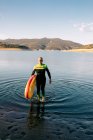 Surfista masculino de fato de mergulho andando com prancha SUP amarela e remo na praia de areia perto da água do mar — Fotografia de Stock