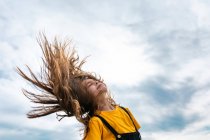 Vista lateral desde abajo de adolescente pacífico lanzando pelo largo en el fondo del cielo nublado en verano - foto de stock