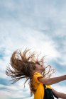 Seitenansicht von unten von friedlichem Teenager, der lange Haare auf wolkenverhangenem Himmel im Sommer wirft — Stockfoto