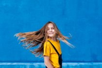 Delighted dreamy teenager with long flying hair standing looking away on blue background — Stock Photo