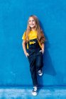 Joyeux hipster adolescent avec bouquet de fleurs jaunes dans la poche de denim globalement appuyé sur le mur bleu et regardant loin — Photo de stock