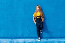 Allegro hipster adolescente con mazzo di fiori gialli in tasca di denim in generale appoggiato sulla parete blu e guardando altrove — Foto stock