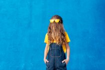 Anonymous cool teenager wearing yellow sunglasses on long hair covering face on blue background — Stock Photo